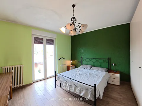 Camera da letto matrimoniale con parete verde e accesso al balcone